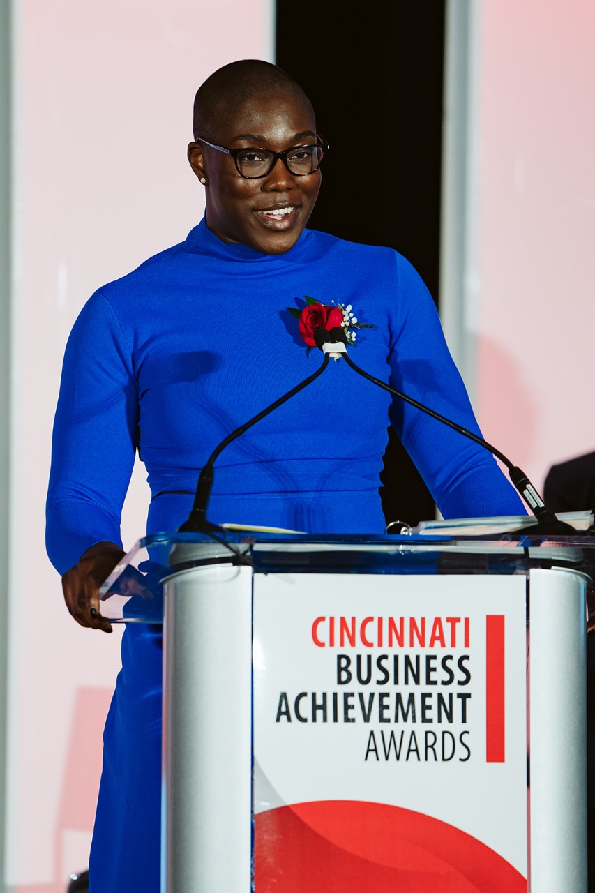 A woman in a blue dress speaks at a podium.