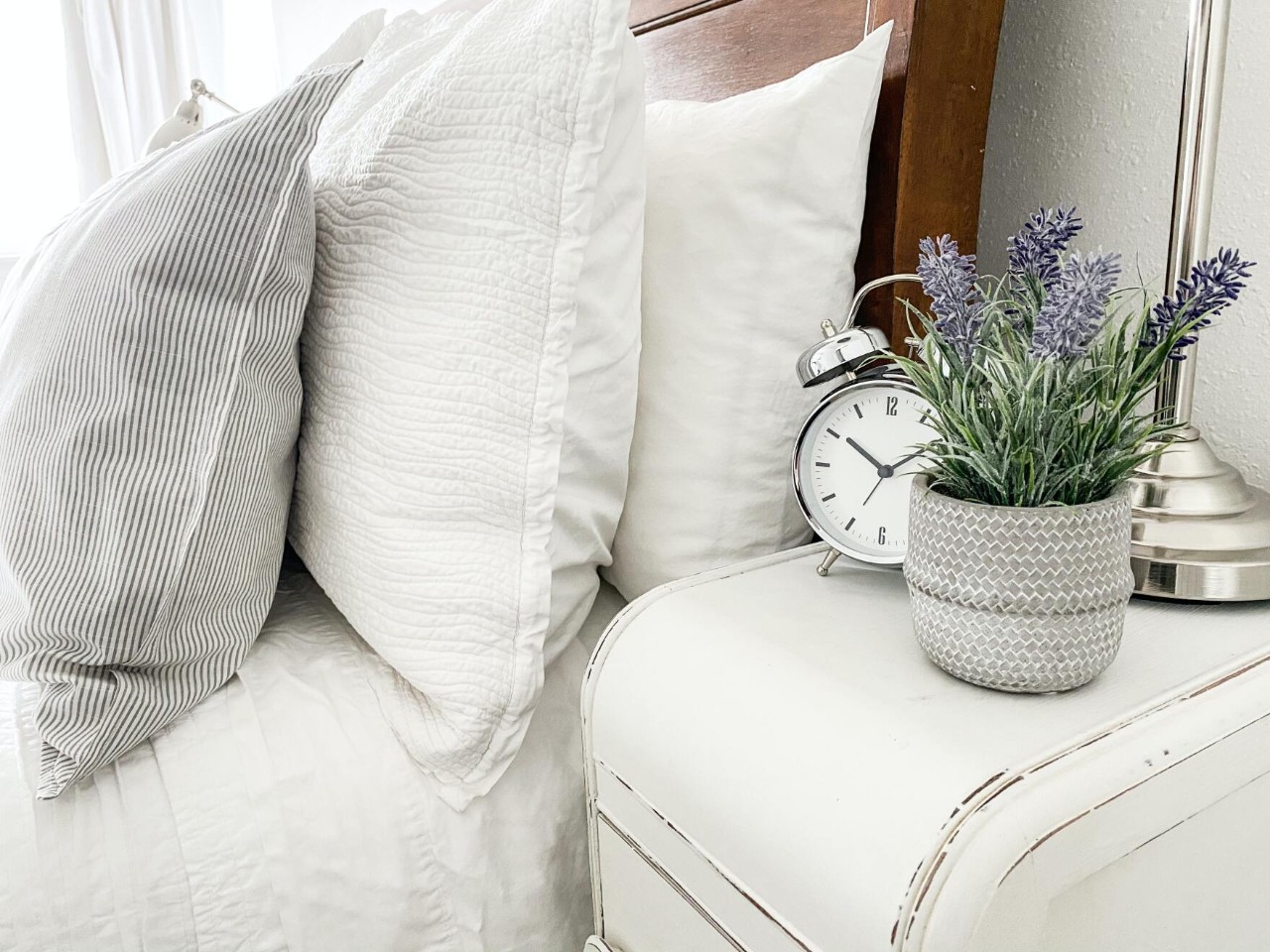 a photo of a made bed with a clock on a nightstand
