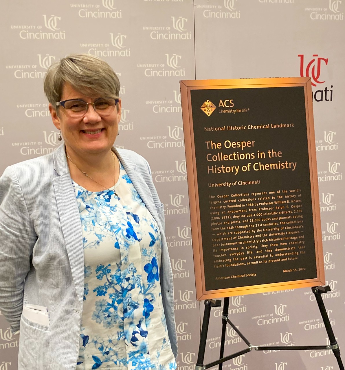 Anna Gudmundsdottir stands next to a plaque dedicating the Oesper Collections as a National Chemistry Historic Landmark.