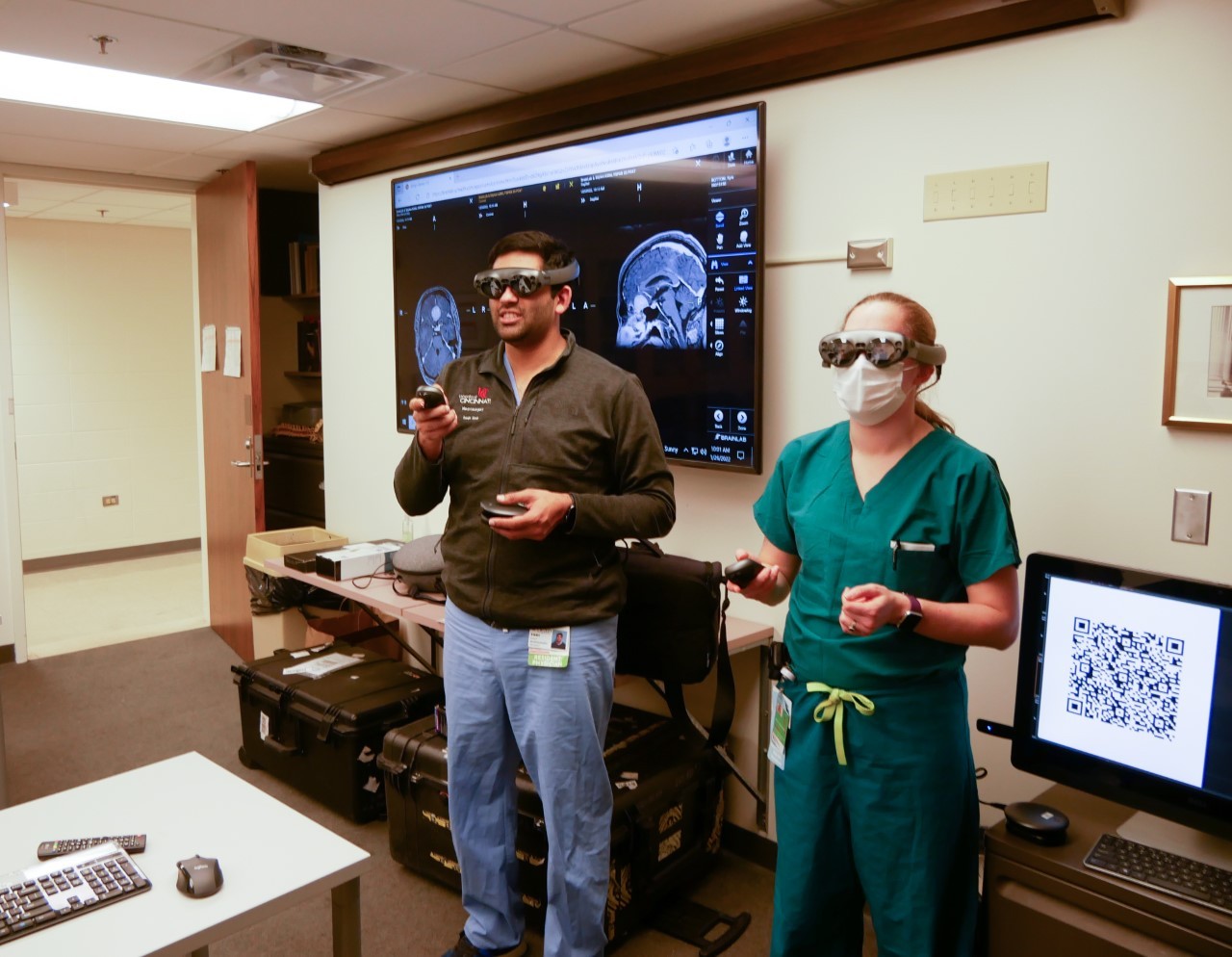 Two students in scrubs stand with goggles over their eyes and controls in their hands