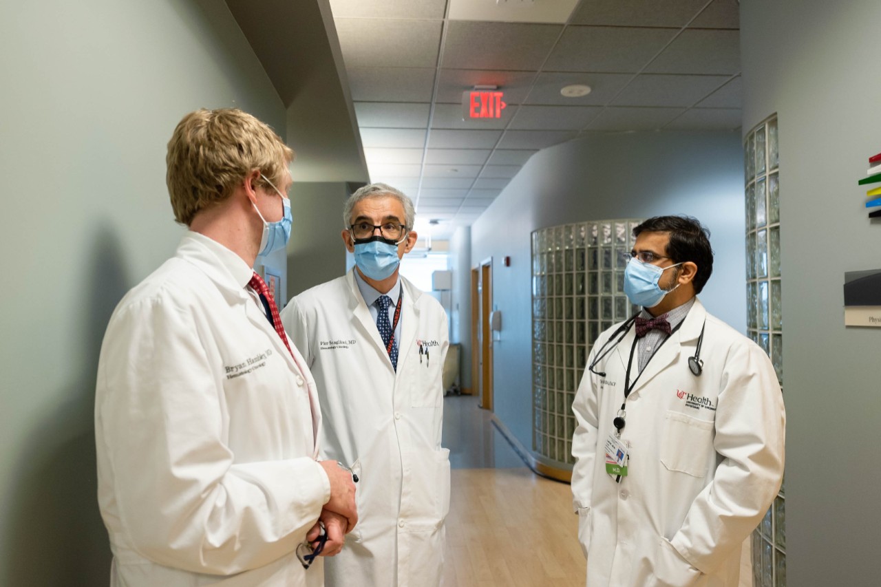 Three doctors wearing lab coats and masks talk in a hospital hallway