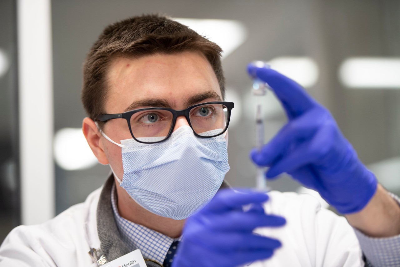 A UC College of Pharmacy student wearing gloves and a face mask draws a COVID-19 vaccine into a syringe.