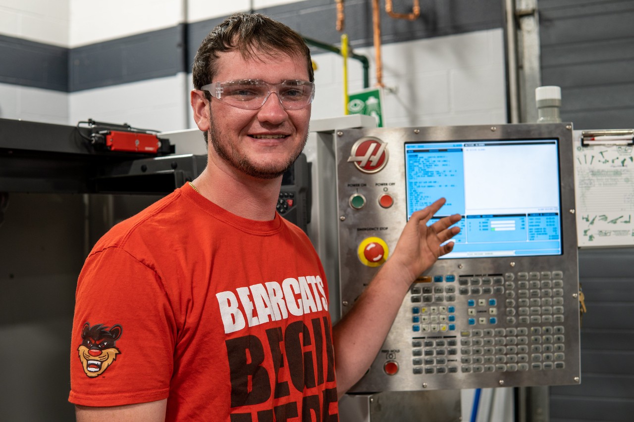 student smiles in front of CNC machine