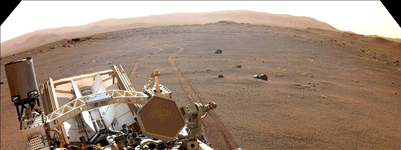 A view looking over Perseverance's body to its tracks in the Martian dirt. 
