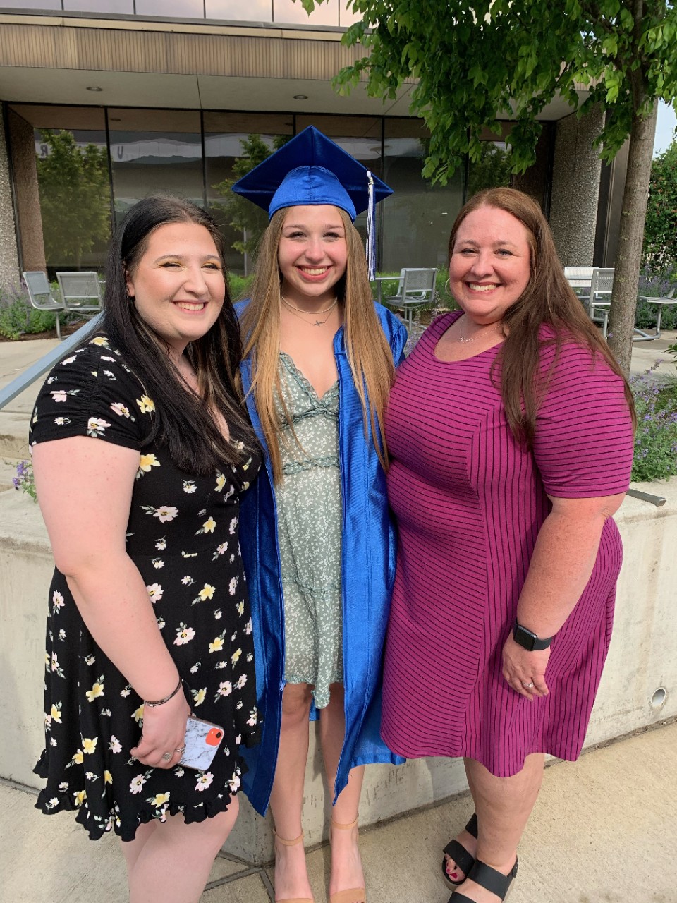 Brooke Bartholomew poses in a graduate cap and gown with her mom and sister.