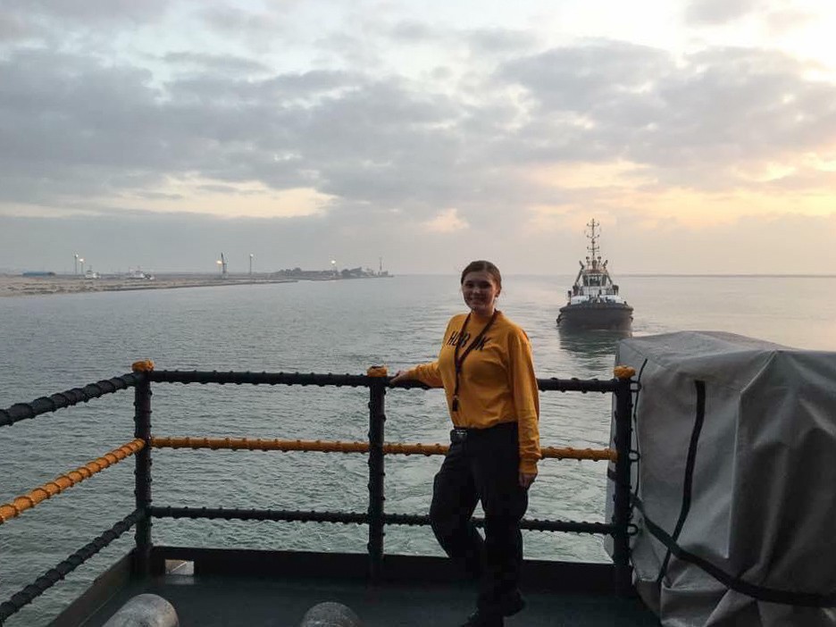 Samantha Orme poses at a railing with a ship behind her.
