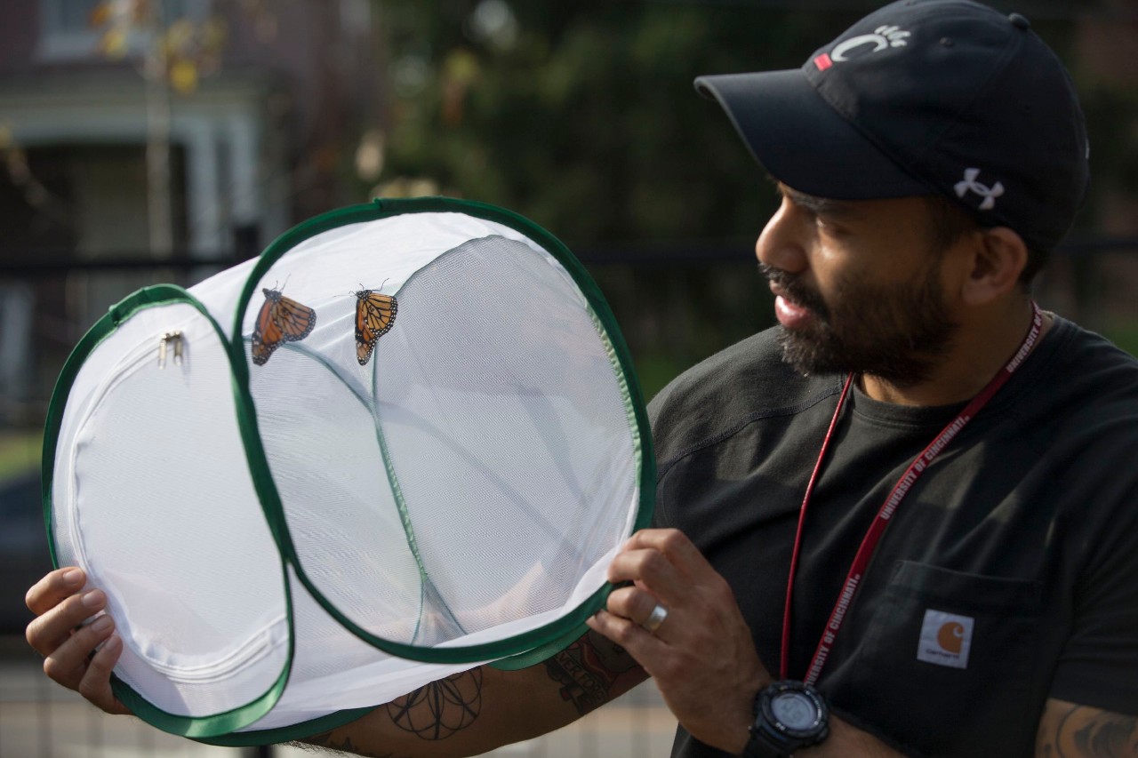 Patrick Guerra holds up a mesh container holding a butterfly,