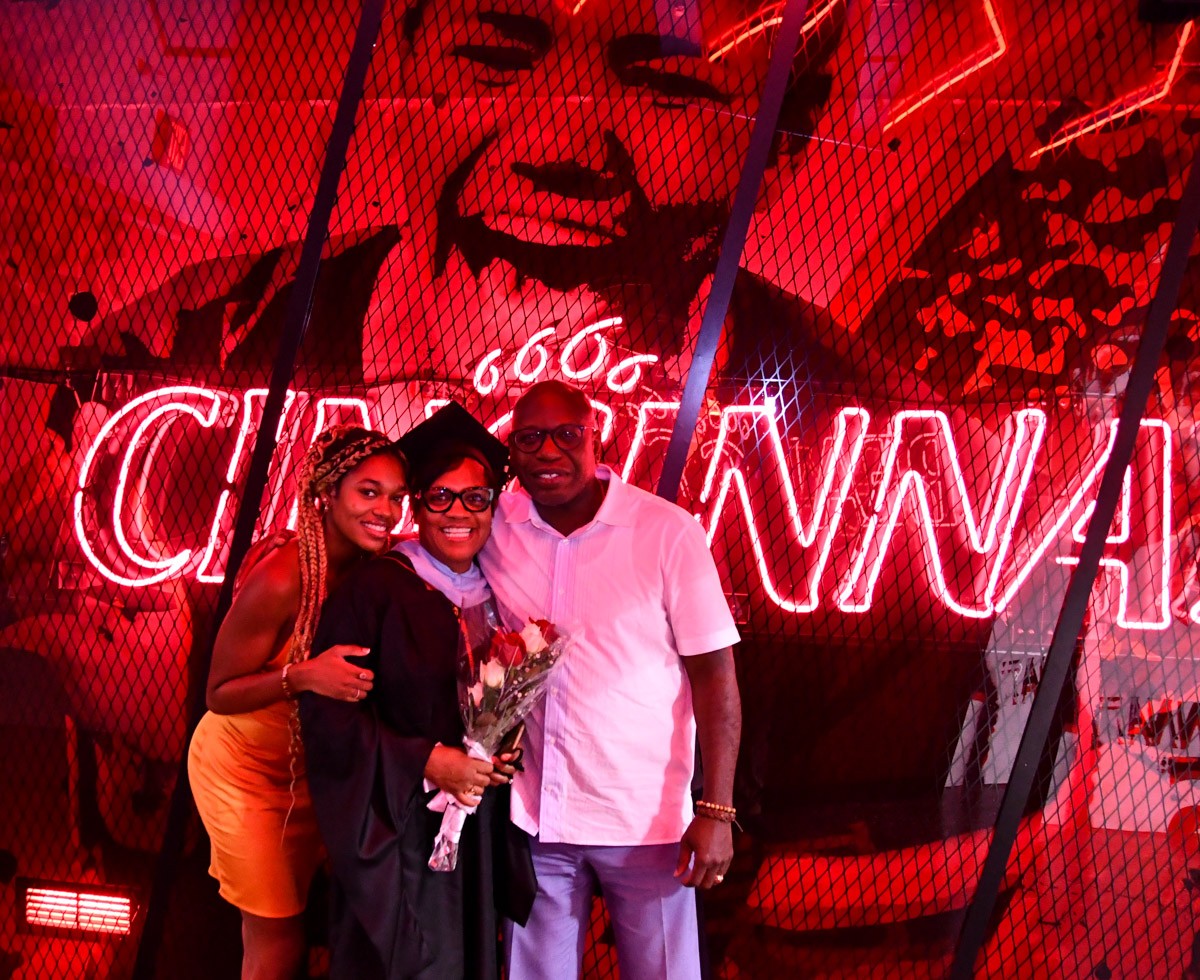 A UC grad poses with her family in front of the neon Cincinnati sign at Fifth Third Arena.