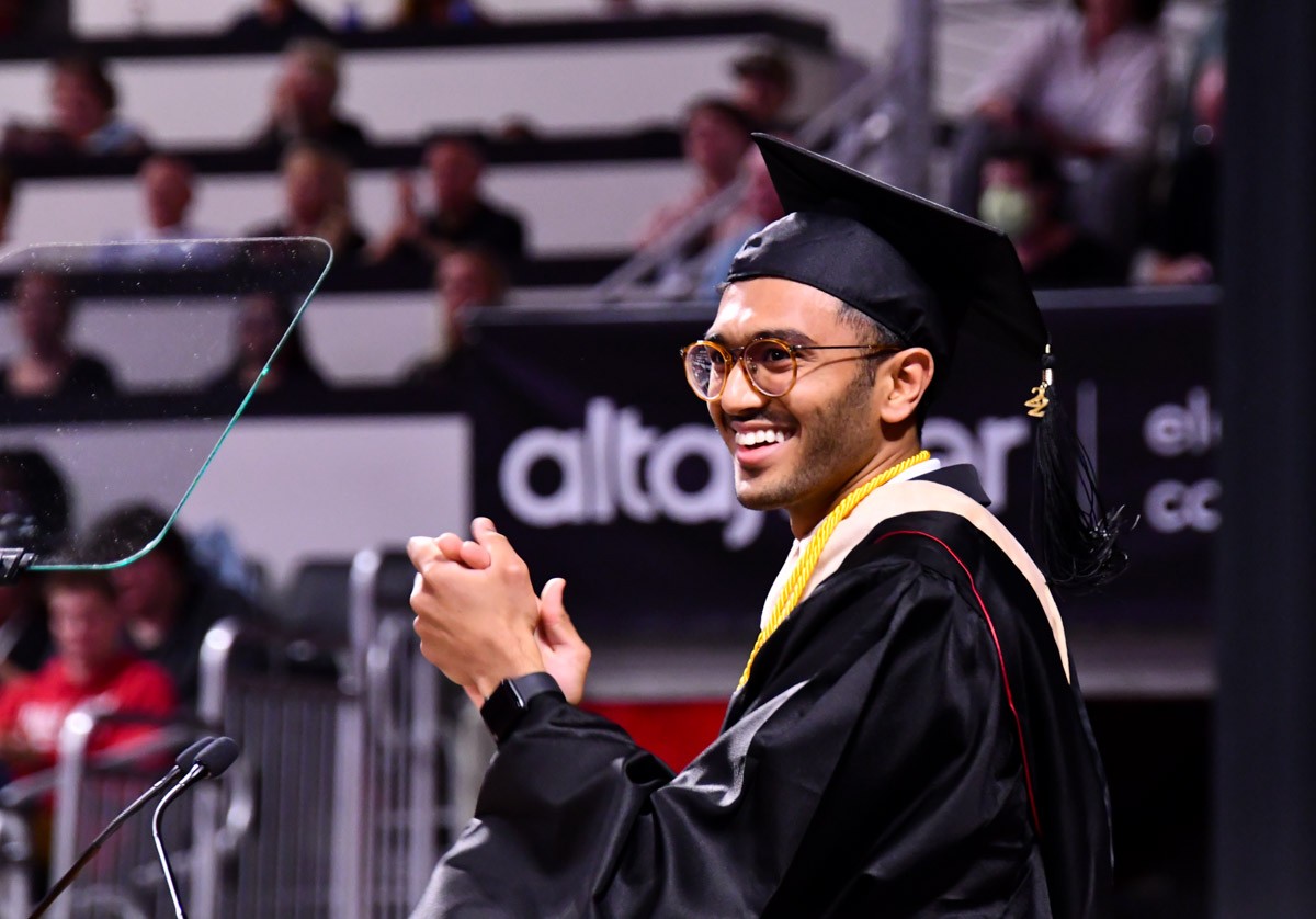 Teja Bollimunta in a black cap and gown applauds at the dais at Fifth Third Arena.