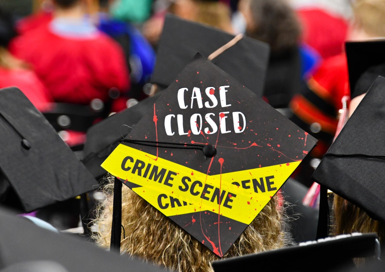 A UC mortarboard is decorated in yellow crime scene tape with the words 'case closed.'