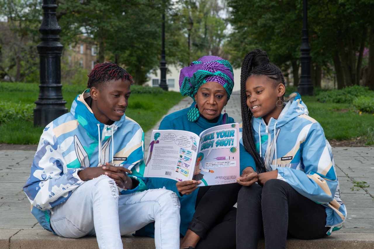 a photo of people sitting in a park reading COVID-19 vaccine information