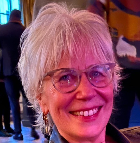 woman with short blonde hair in glasses smiles at a crowded event