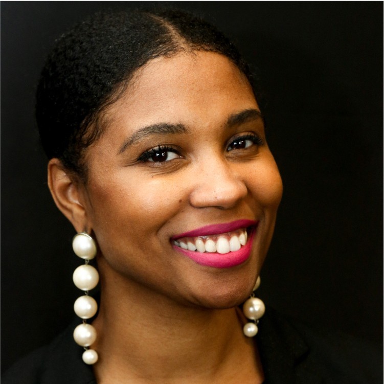 black woman with white drop earrings smiles for a headshot against a black background
