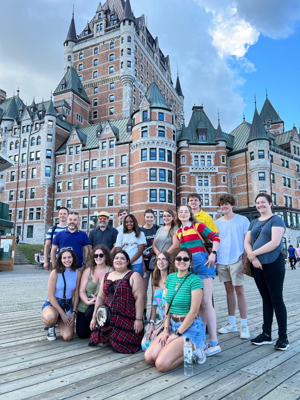 A group of people pose on a boardwalk in front of a large and elaborately turreted brick and stone building