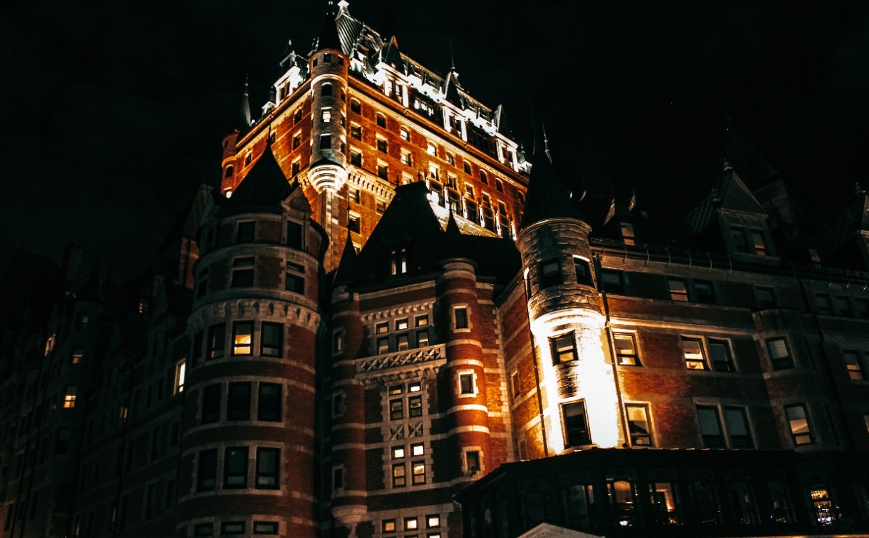 A dramatically uplit photo of the Chateau Frontenac at night, the turrets and upper gables and dormers spotlit