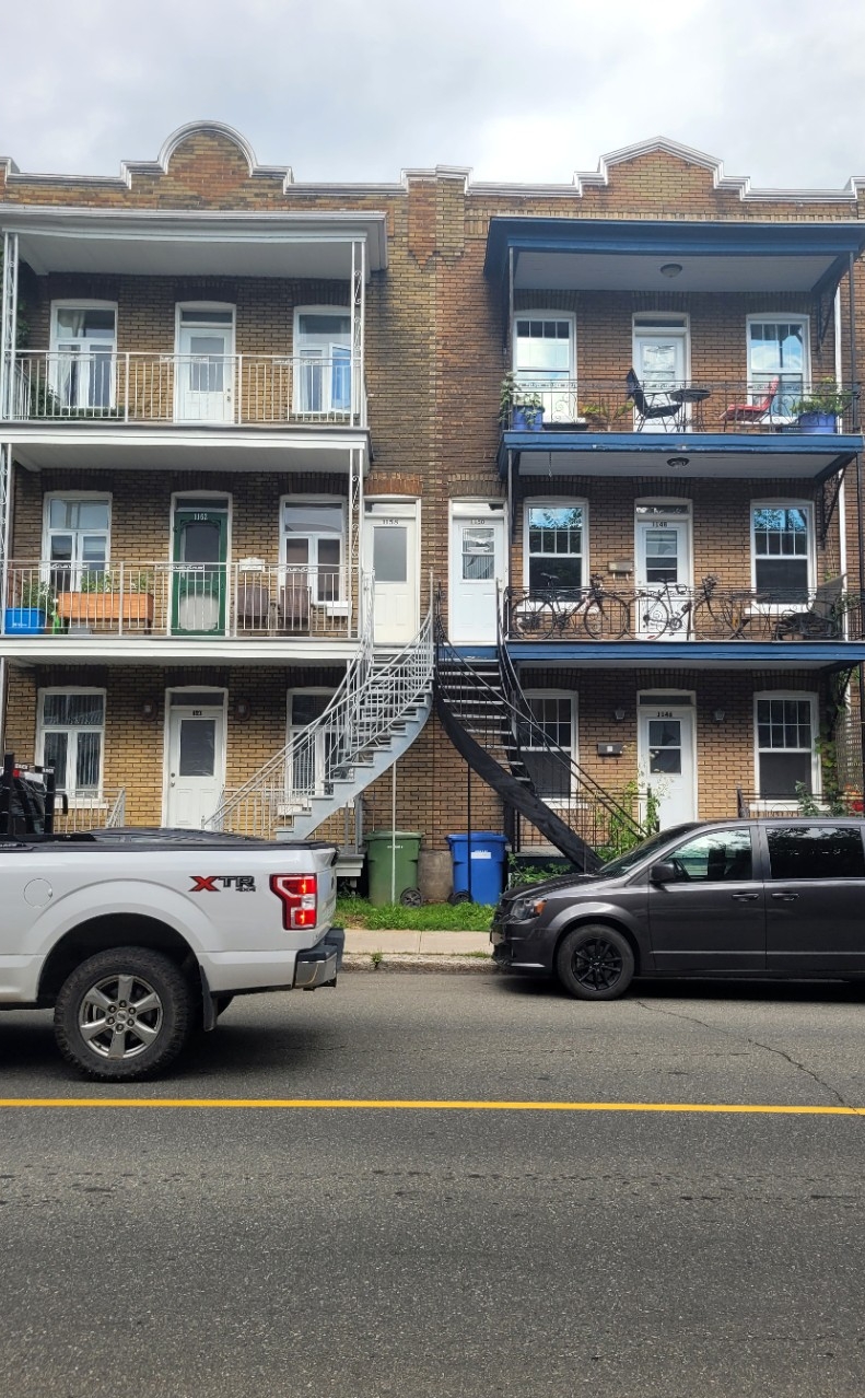 A duplex with curving staircases and balconies, one side painted white, one black, with a white truck driving by in front of the white side and a black SUV parked in front of the black side
