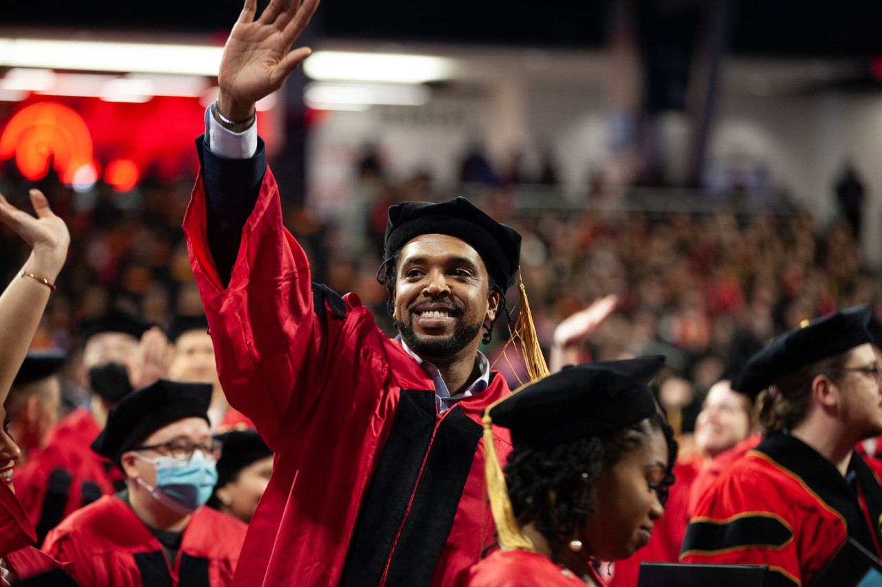 A grad in a cap and gown waves from the floor of Fifth Third Arena.