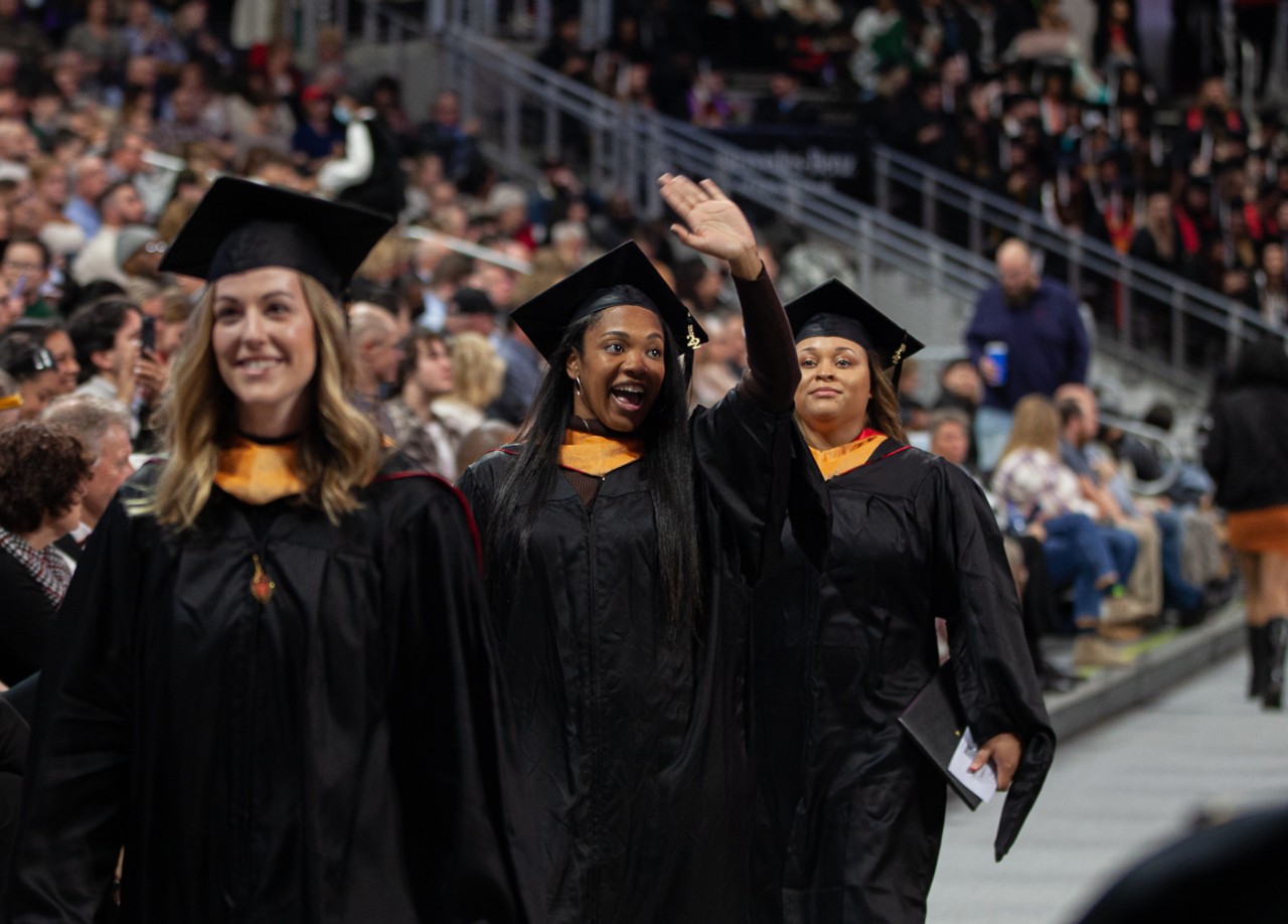 A graduate waves while walking during commencement.