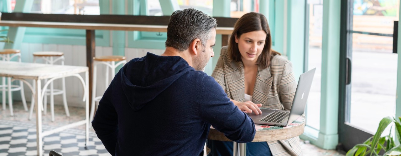 Two people sitting at table with laptop discussing taxes.
