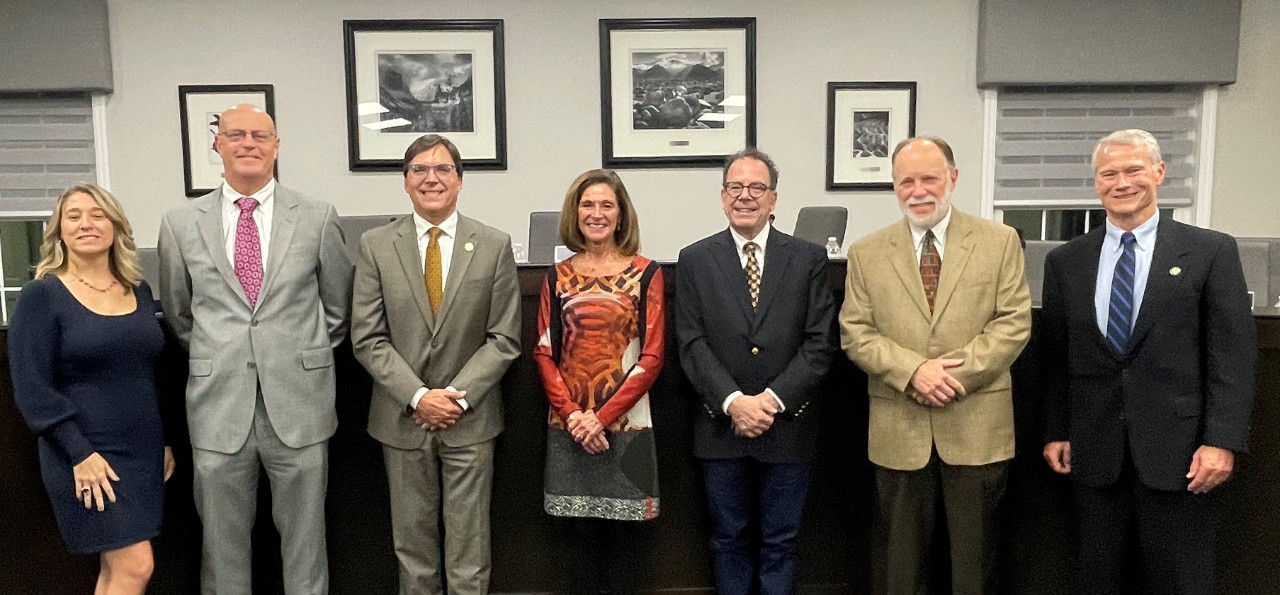 two men and five women in business attire pose in a row in the city council chamber