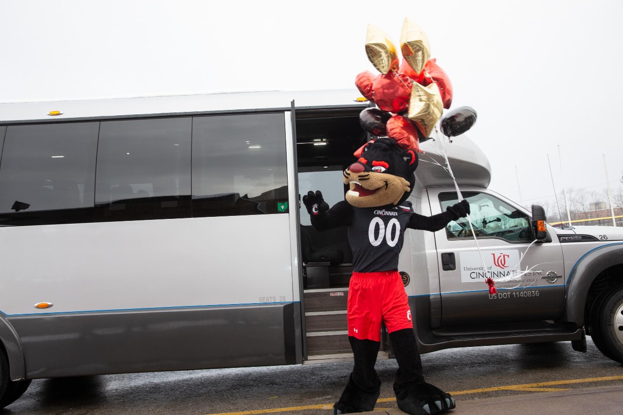 Bearcat mascot holds balloons in front of shuttle bus