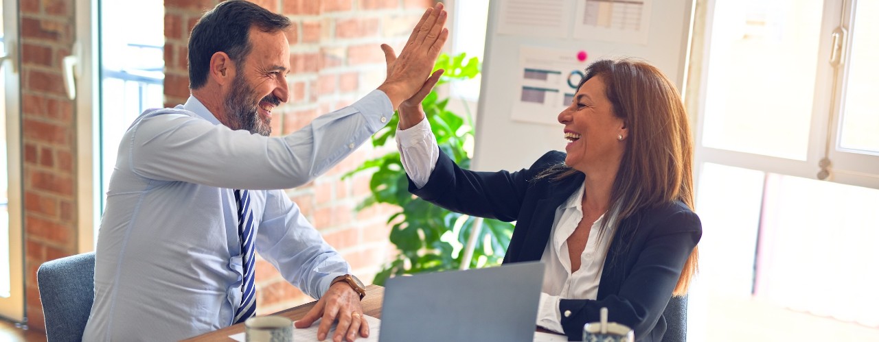 Man and woman give high five in air over a laptop on a table.