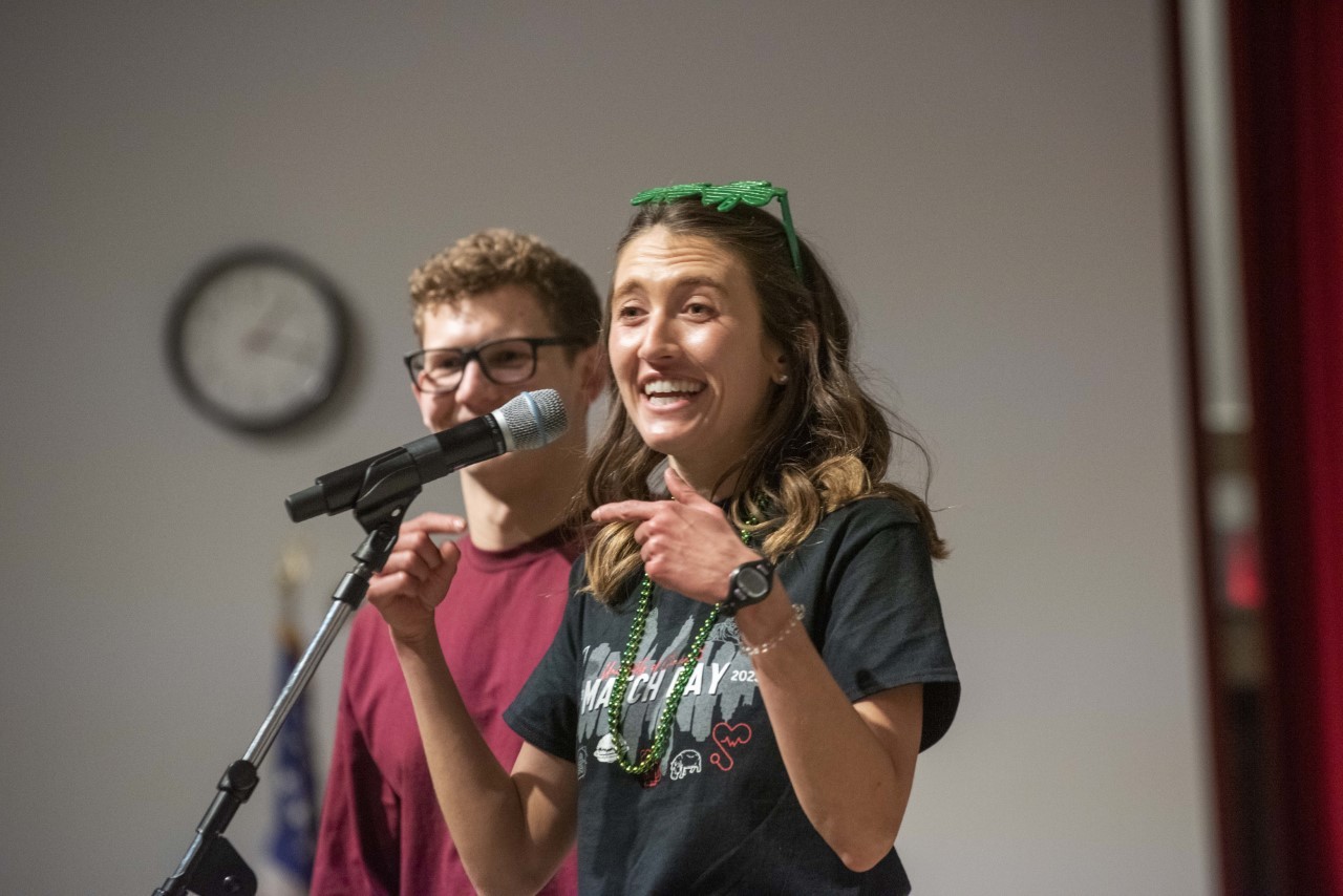 Rachel Holloway smiles in front of a microphone with her boyfriend behind her