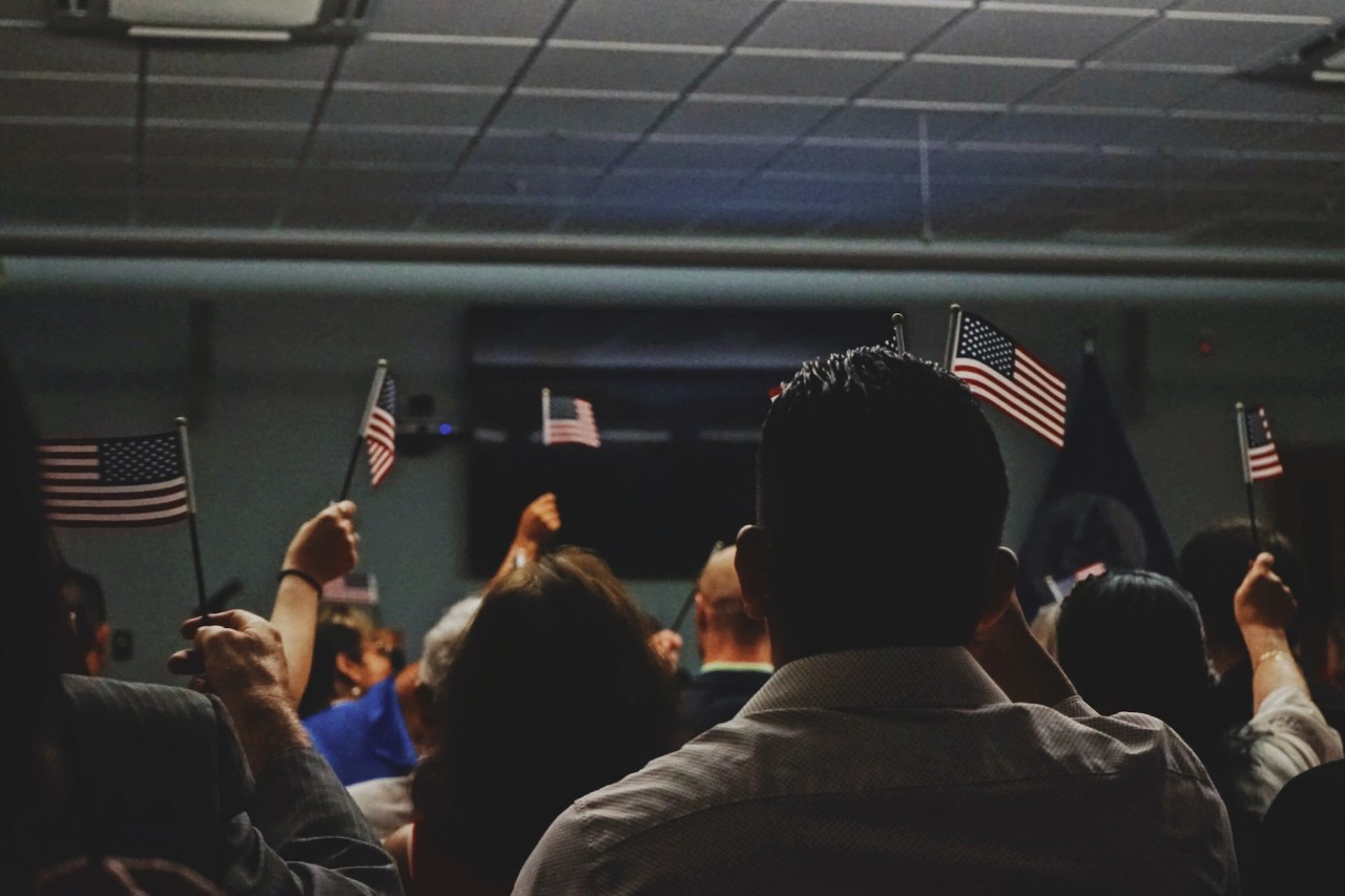 the backs of people sitting  in a room holding American flags  