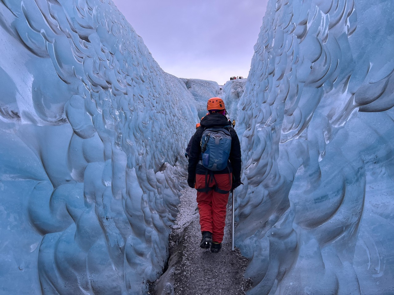 A person with their back to the camera hikes through a glacier ridge.