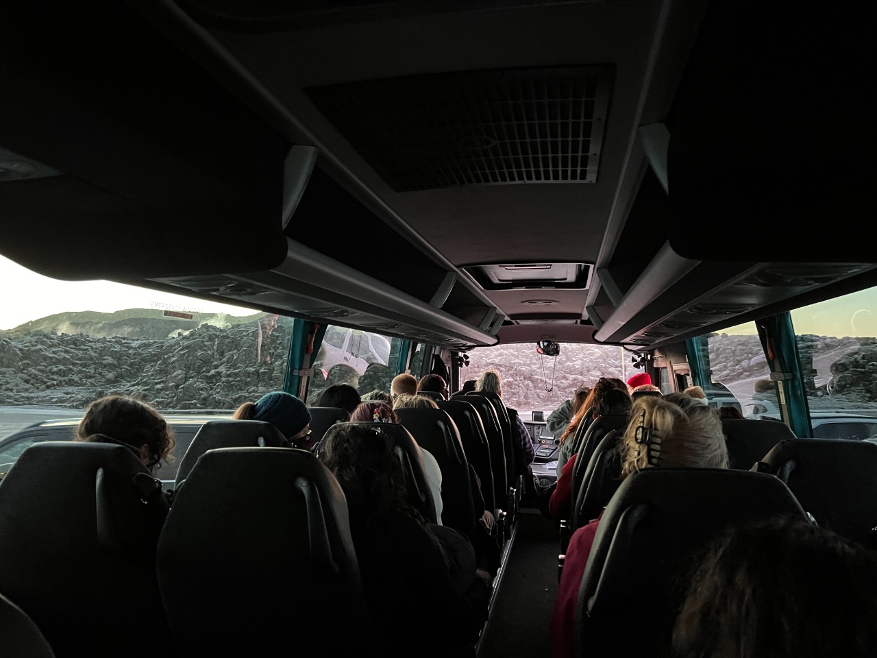 People sit on a bus. Outside the window is the landscape of Iceland.