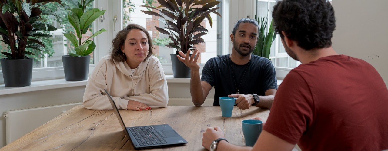 Three adults sitting at table with a laptop.