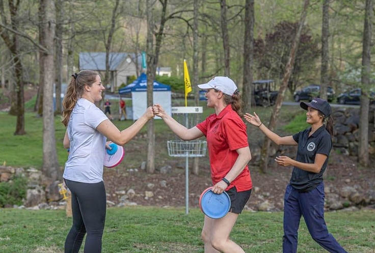 Two players fist-bump while retrieving their discs from a basket.