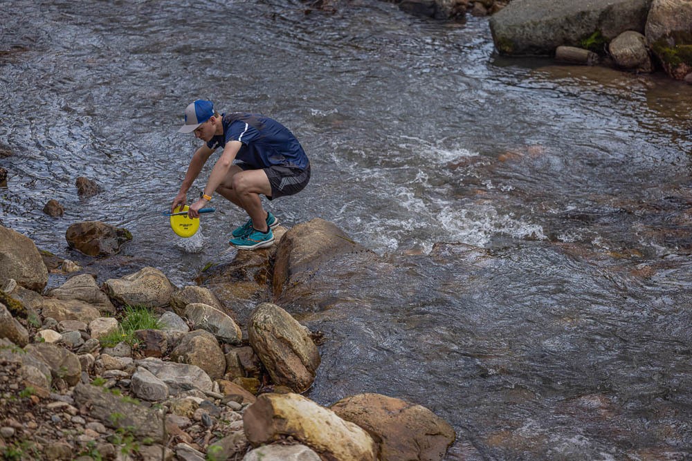 A player squats to retrieve a disc from a stream.
