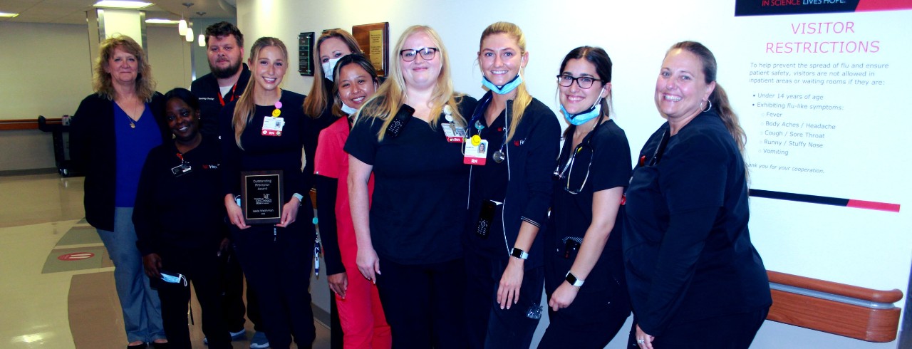 Lexie Weithman holding a comemmorative plaque and standing with coworkers at UC Medical Center