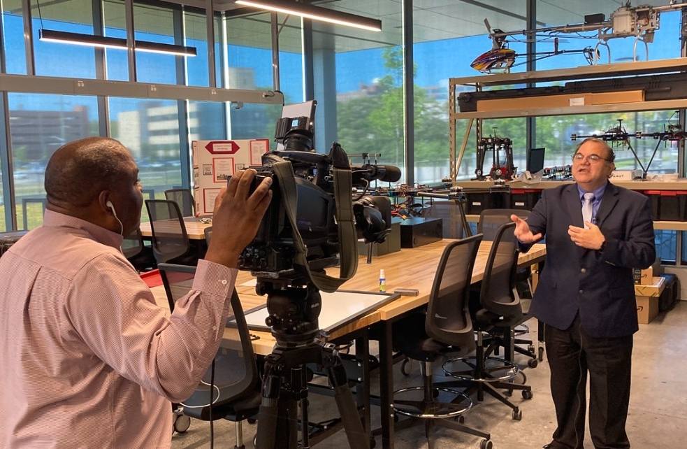 A reporter with a video camera talks to Kelly Cohen in a lab.