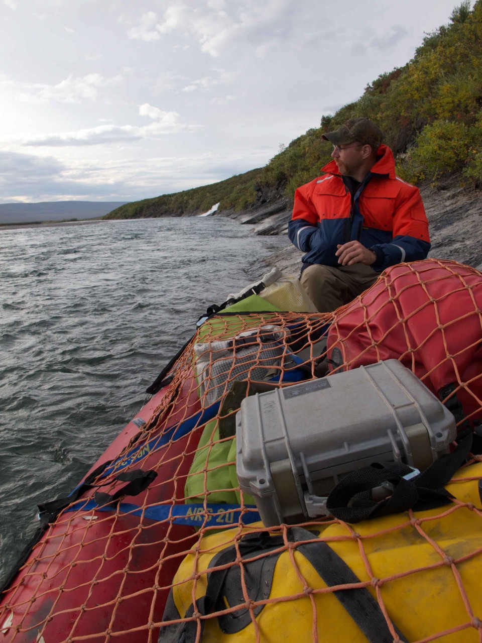 A researcher in a boat full of gear cruises along a river in Alaska.