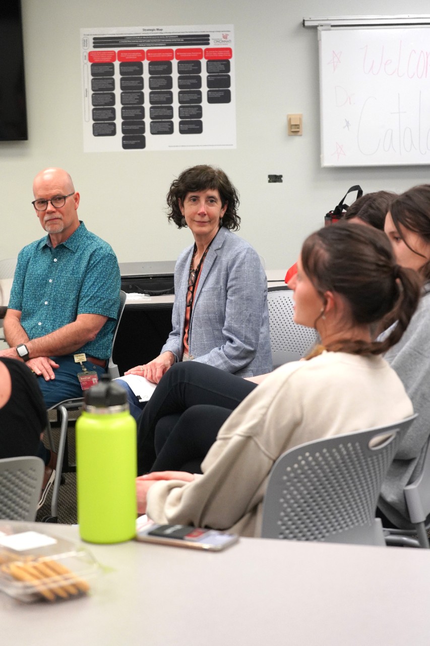 A man and woman sit in a classroom, listening to a circle of students