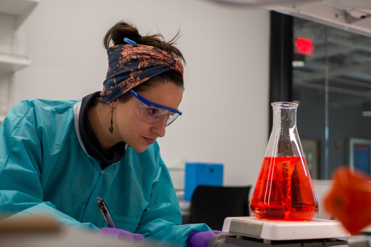 UC graduate student Carolyn Nietupski looking at a beaker in the UC Bioscience Center.