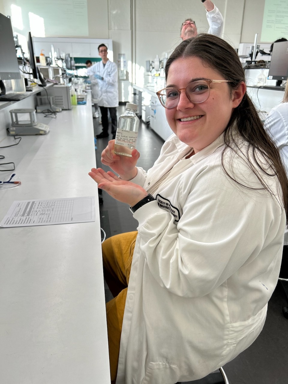 UC Pharmacy student Hannah Fry wears a lab coat and holds a glass bottle filled with clear liquid in a lab.