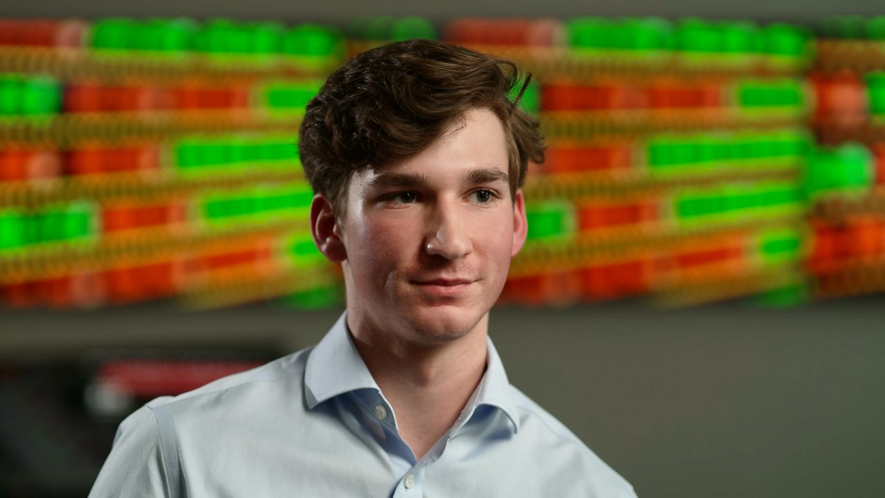 Portrait of UC business student Patrick McNamara in front of an investment trading screen.