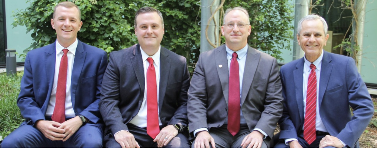 1819 Wealth Advisors, dressed in dark suits and red ties, stand in the courtyard of Lindner Hall.