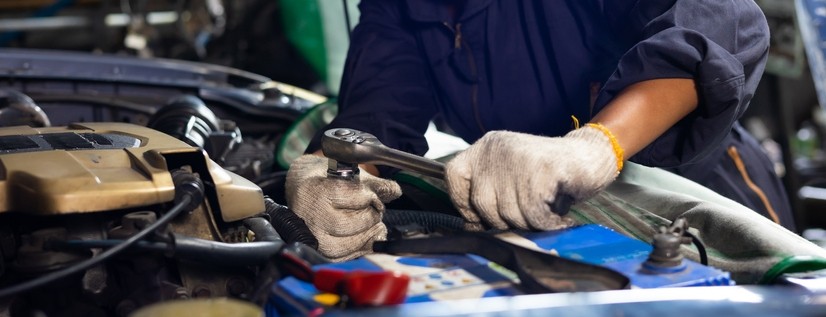 A car mechanic checking and fixing a car engine at a service garage.