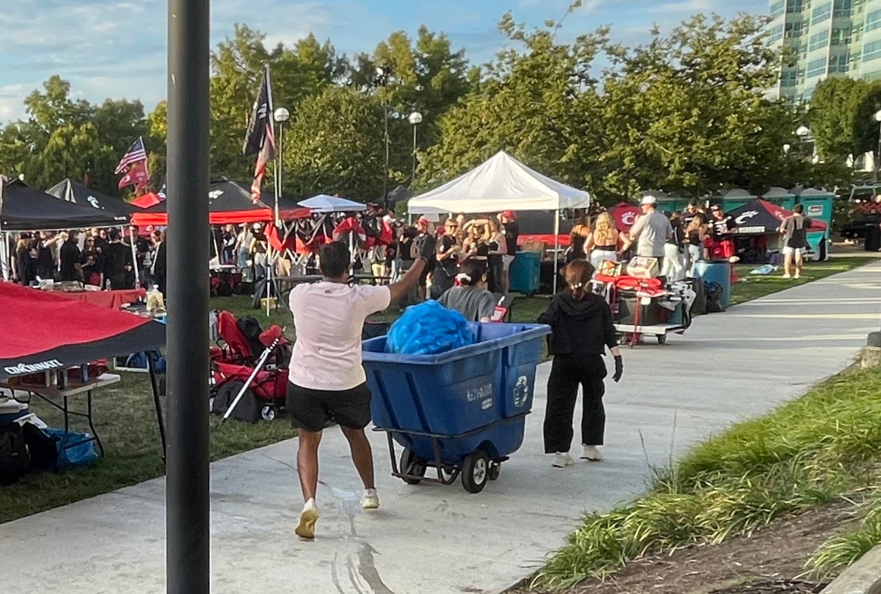 UC student volunteer tosses a large blue bag of recyclables into a large blue rolling cart.