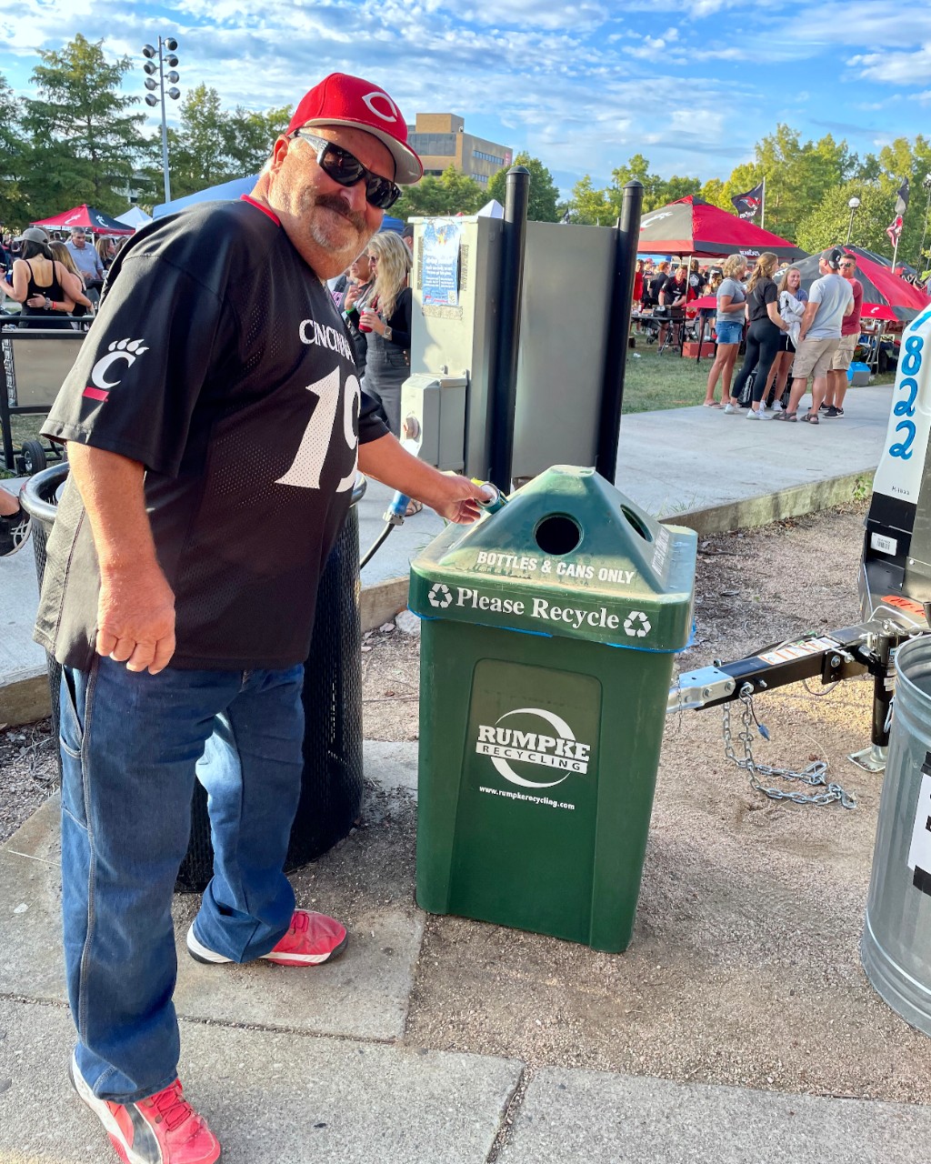Man wearing a UC Bearcat shirt tosses a can into a green campus recycle can.