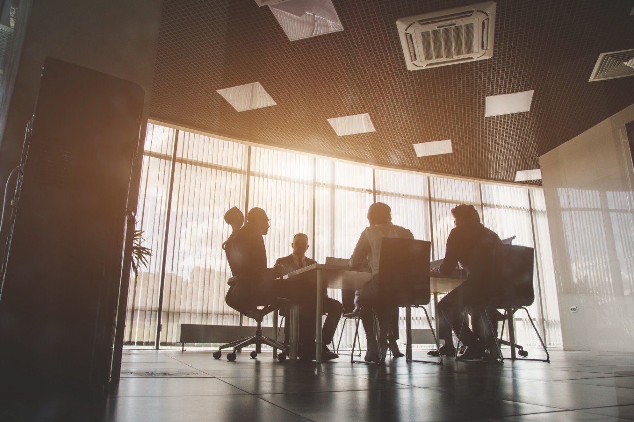 Silhouettes of people sitting at the table. A team of young businessmen working and communicating together in an office. Corporate businessteam and manager in a meeting.