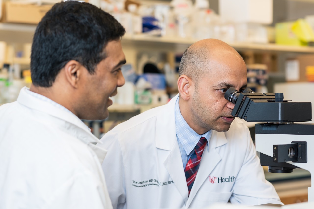 Davendra Sohal looks into a microscope while Krushna Patra looks on