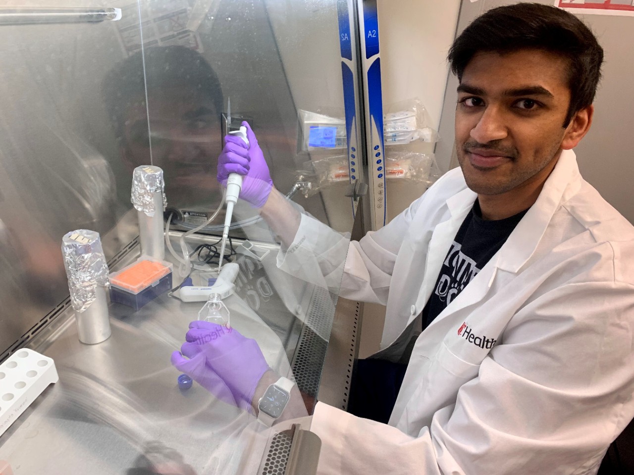 Rohan Rao holds a pipette under a laboratory hood