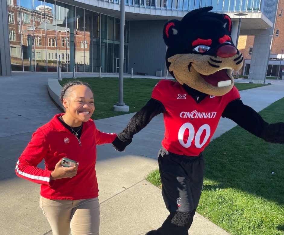 Ronay skips around the outside of the HSB with UC's mascot. 