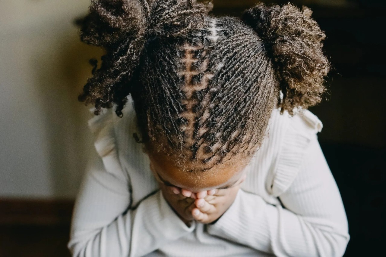 young black person with hands covering her face