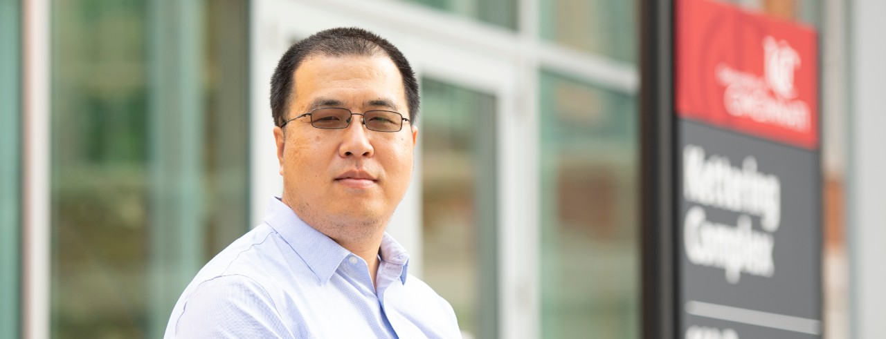 Headshot photo of Jun Wang standing outside of a building